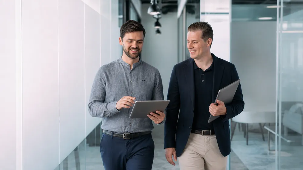 Twee zakelijke professionals lopen over een kantoor en bekijken een tablet
